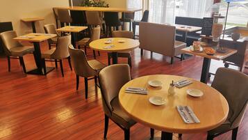 A restaurant with round tables and chairs, wooden flooring, and a menu board visible.