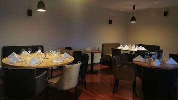A restaurant with round tables, chairs, and pendant lighting.