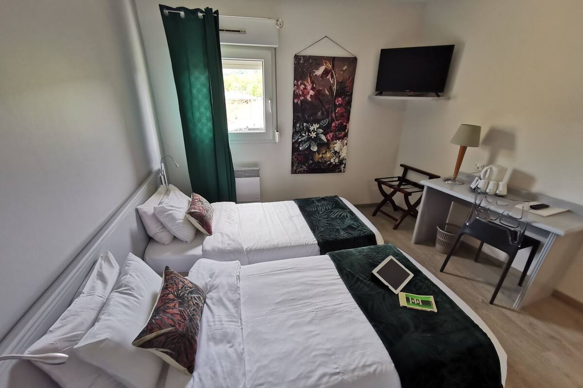 Habitación de hotel con dos camas, un escritorio, una silla, un televisor y una ventana con cortinas.
