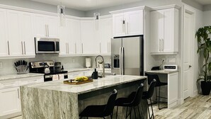 A modern kitchen with white cabinets, a marble island, black bar stools, and stainless steel appliances.