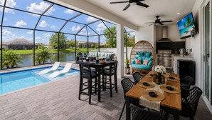 A pool area with a table and chairs, a hanging chair, and a kitchen area with a TV.