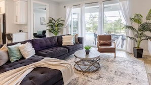 A modern living room with a dark-colored sofa, a round coffee table, and a large window offering a view of the outdoors.