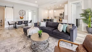 A spacious living room with a dark grey sofa, a round coffee table, and a dining area with a white table and chairs.