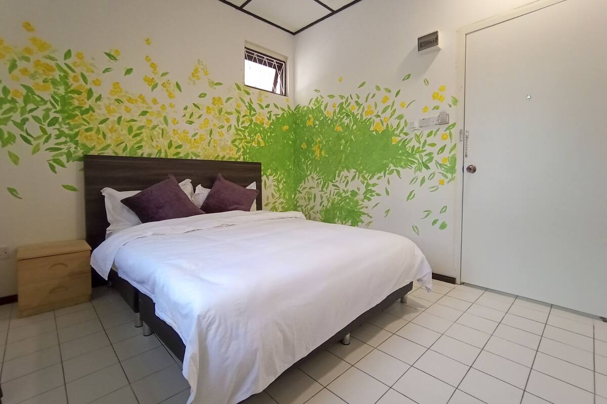 A neatly made bed with white linens and purple pillows in a room with a tiled floor.