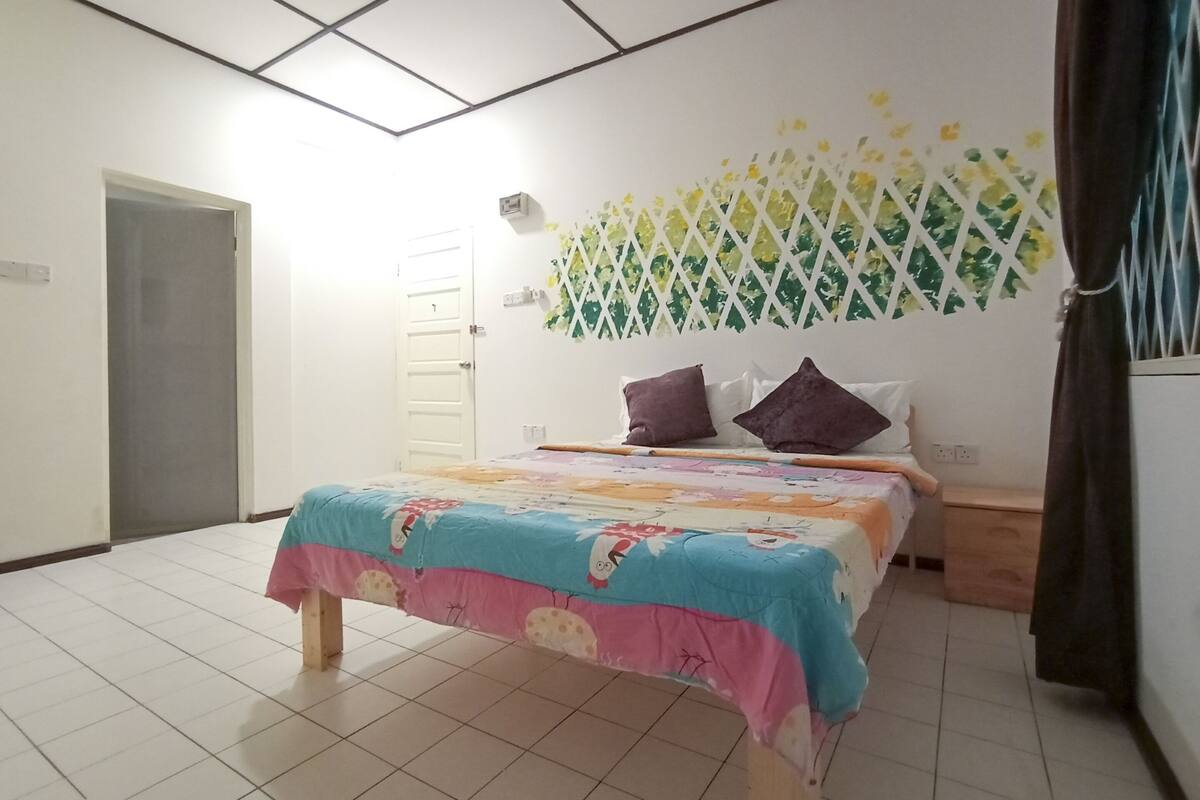A bedroom with a bed, a door, a wall-mounted air conditioner, and a window with curtains.