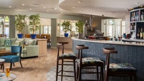 Un moderno vestíbulo de hotel con zona de bar, asientos y amplias ventanas.