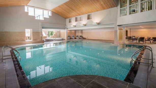 Una amplia piscina interior con agua cristalina y azul, rodeada de tumbonas y una terraza soleada.