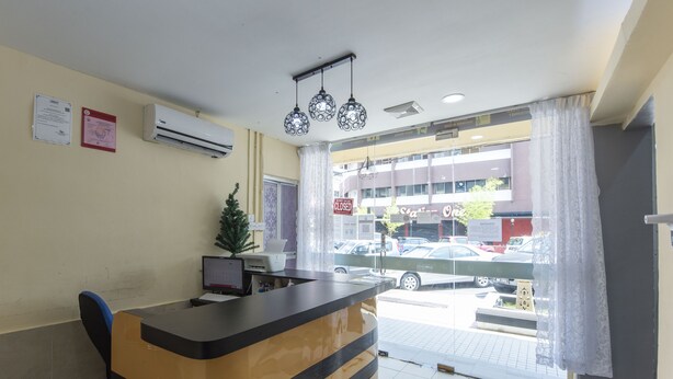 A reception desk with a computer, a small plant, and a window with a view of parked cars and a building outside. - OYO 90254 D Anugerah Hotel (Malacca City)