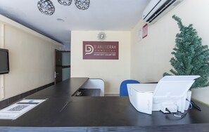 A reception area with a dark reception desk, a mounted air conditioner, a decorative wall piece, and a small Christmas tree.