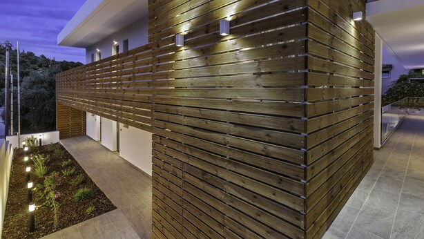 A modern building with horizontal wooden slats, a tiled patio, and outdoor lighting. - Sigma Luxury Rooms (Igoumenitsa)