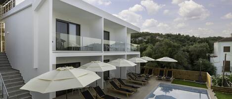 Un edificio moderno con piscina, tumbonas y sombrillas.
