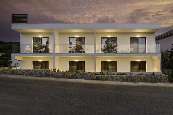 A modern two-story house with a balcony, stone foundation, and multiple windows. - Sigma Luxury Rooms (Igoumenitsa)