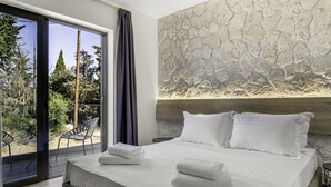 A modern bedroom with a large bed, a stone wall, and a balcony with chairs. - Sigma Luxury Rooms (Igoumenitsa)