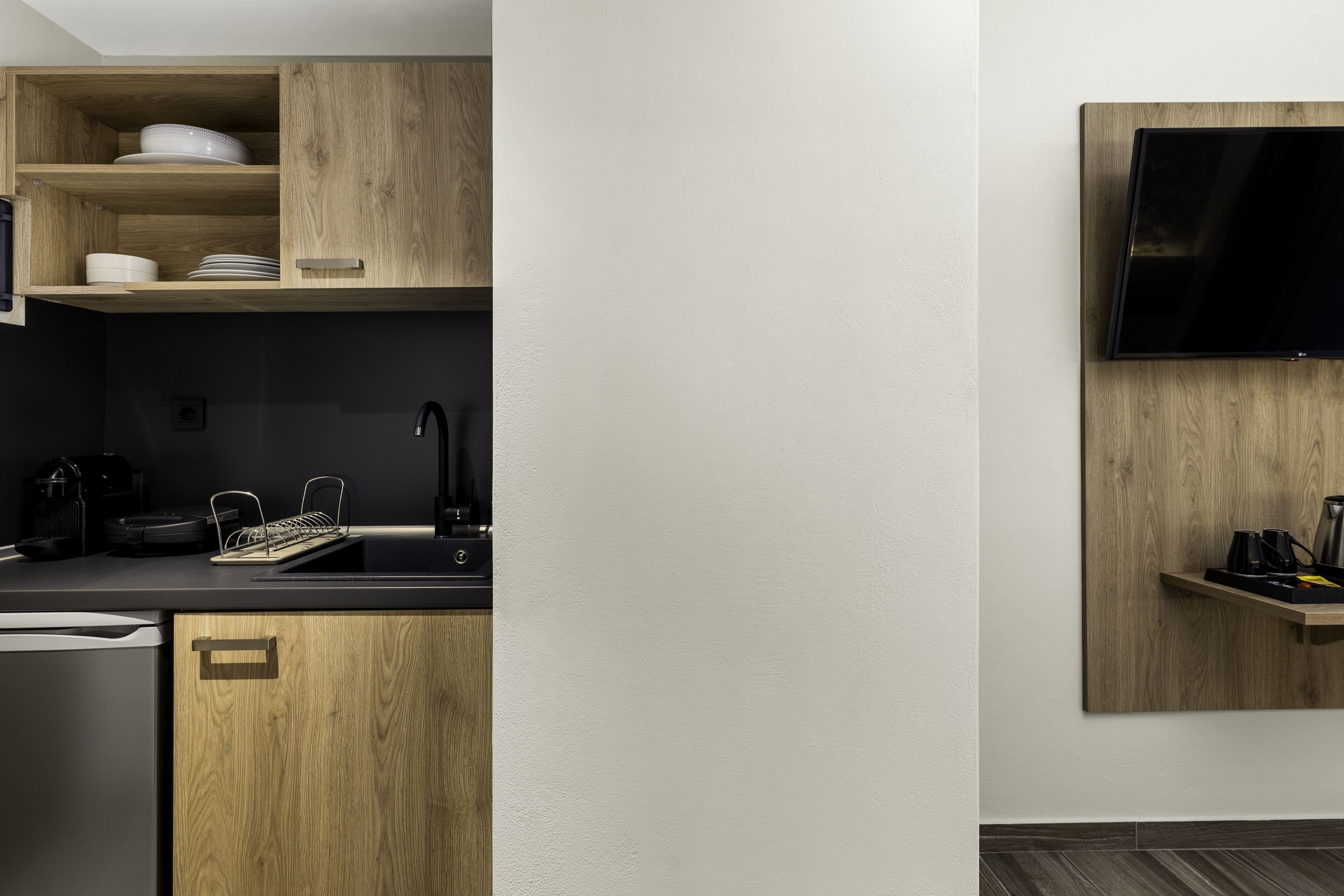 A modern kitchen with wooden cabinets, a black countertop, a built-in dishwasher, and a wall-mounted TV.