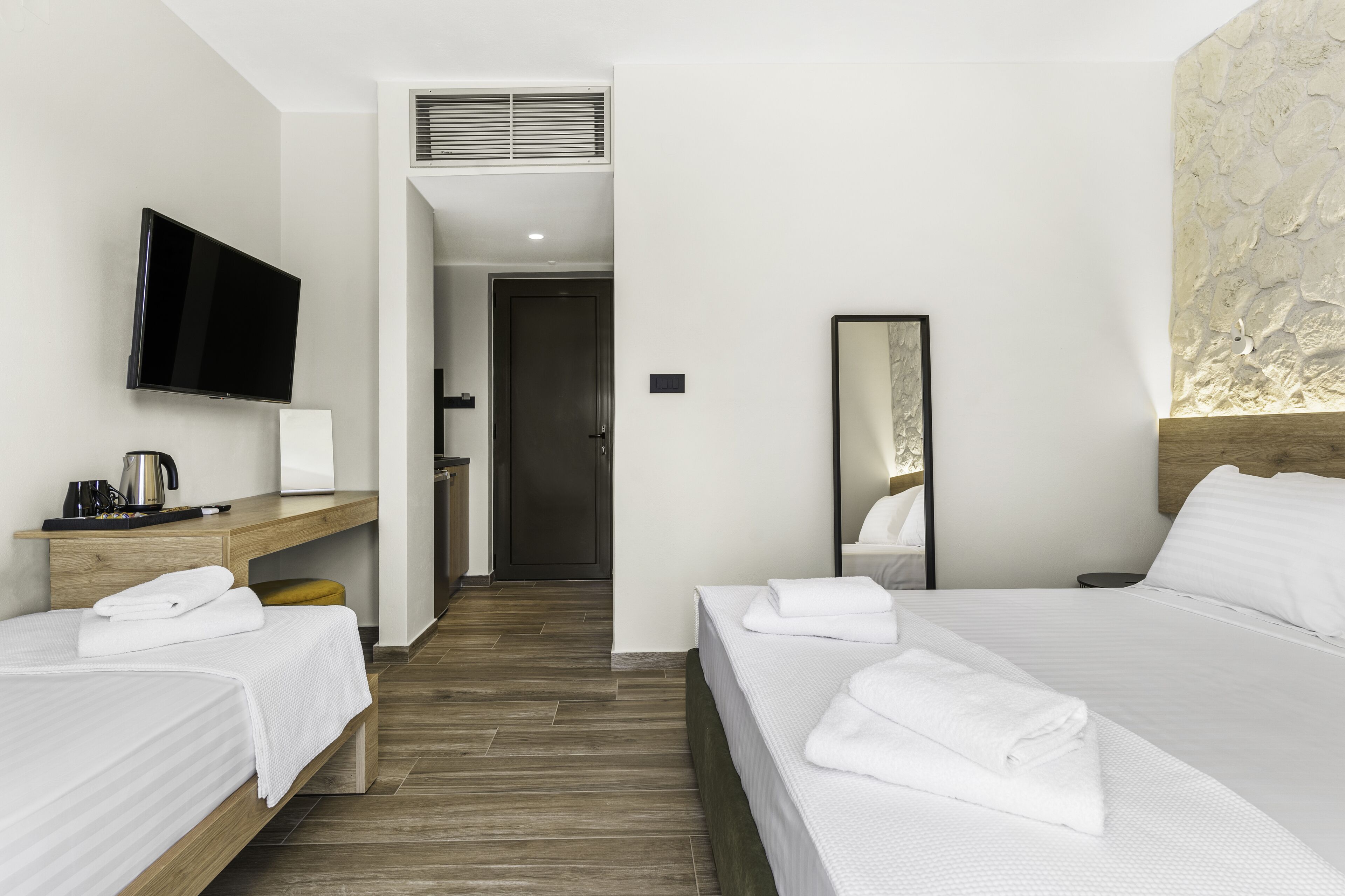 A hotel room with two beds, a TV, a mirror, and a wooden floor.
