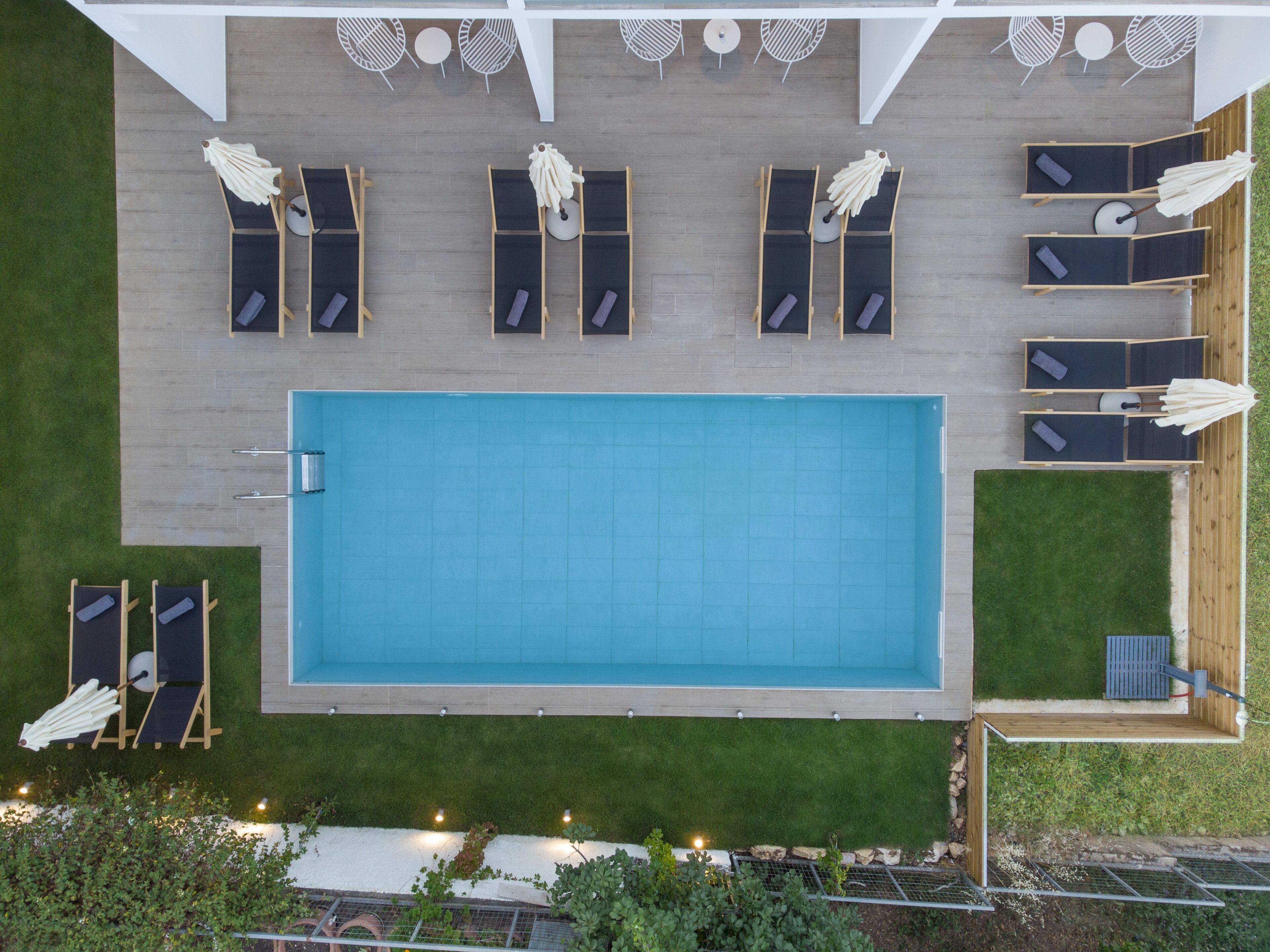 A rooftop pool with sun loungers and umbrellas, surrounded by a wooden deck and a grassy area.