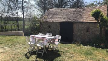An outdoor dining area with a stone building, a table with chairs, and a grassy lawn.