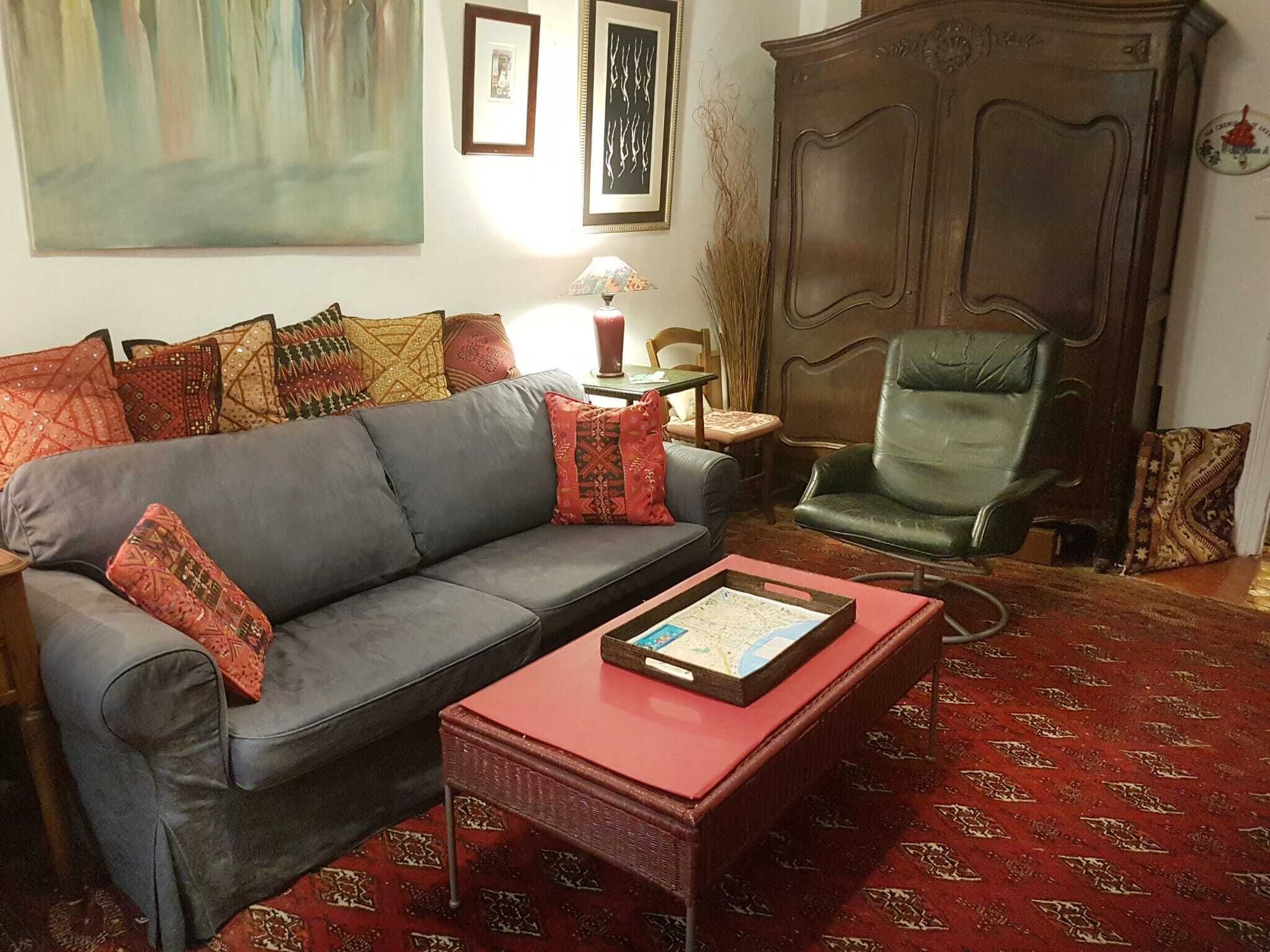 A living room with a grey sofa, a red coffee table, a green armchair, and a patterned carpet.