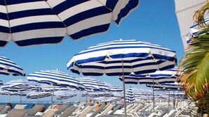 A beach with rows of lounge chairs and blue and white striped umbrellas. - Old Town Nice Family APT  Spacious  2BR;  A/C  3 min walk Beach cafes shops tram (Nice)