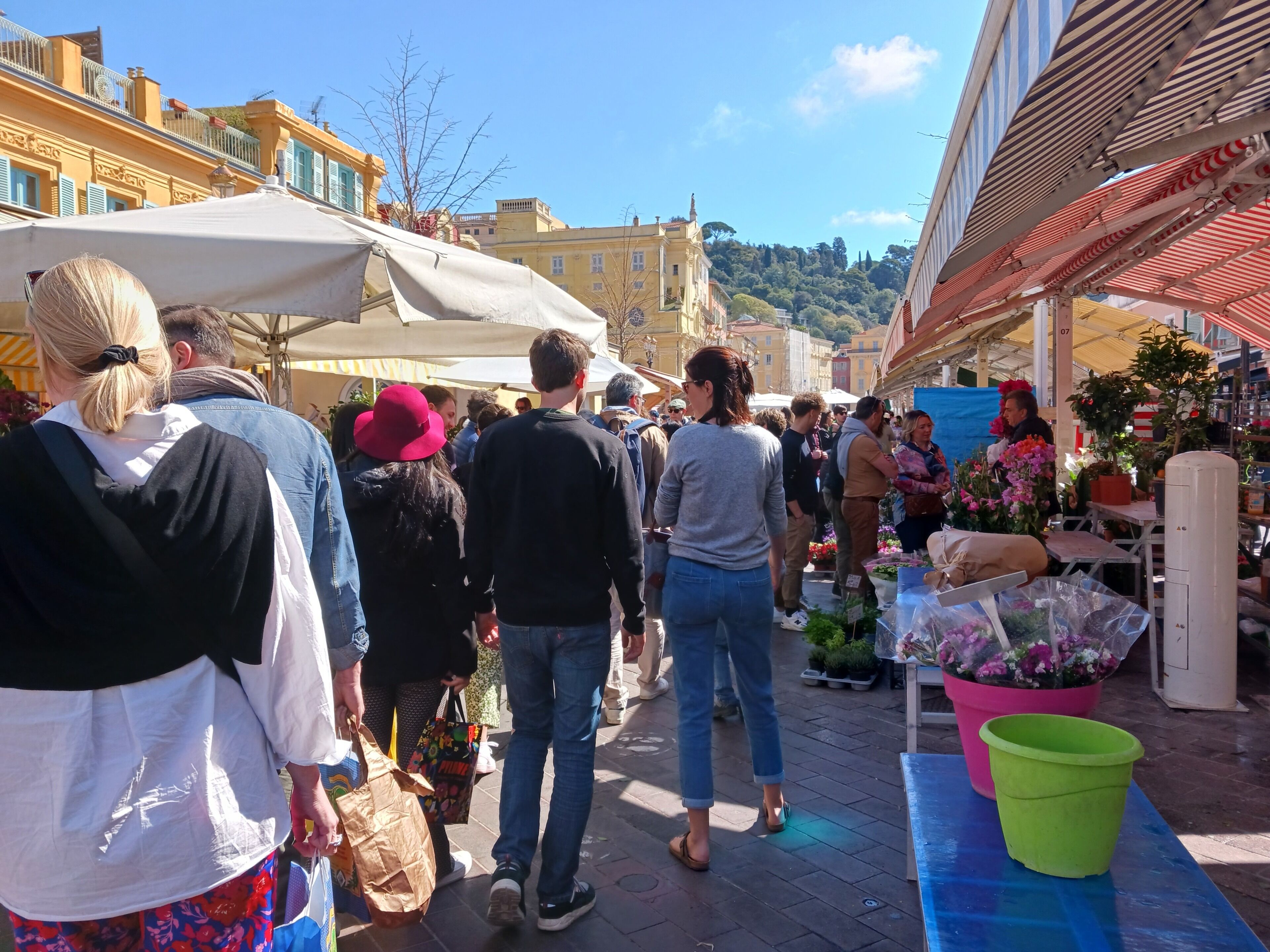 A bustling outdoor market with people walking and vendors selling flowers.