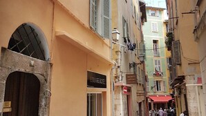 A narrow street with buildings featuring arched windows and shutters. A sign for 'L'OUVRE BOITE' is visible. - Old Town Nice Family APT  Spacious  2BR;  A/C  3 min walk Beach cafes shops tram (Nice)