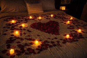 A bed with rose petals and candles arranged in a heart shape.