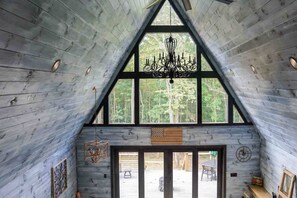 A cabin interior with a high ceiling, wooden walls, a chandelier, and a large window overlooking a forest. - Ultimate Romantic Couples Getaway in Wine Country (Dobson)