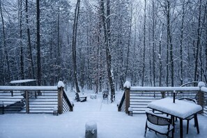 A snow-covered deck with a wooden railing, a bench, and a table.