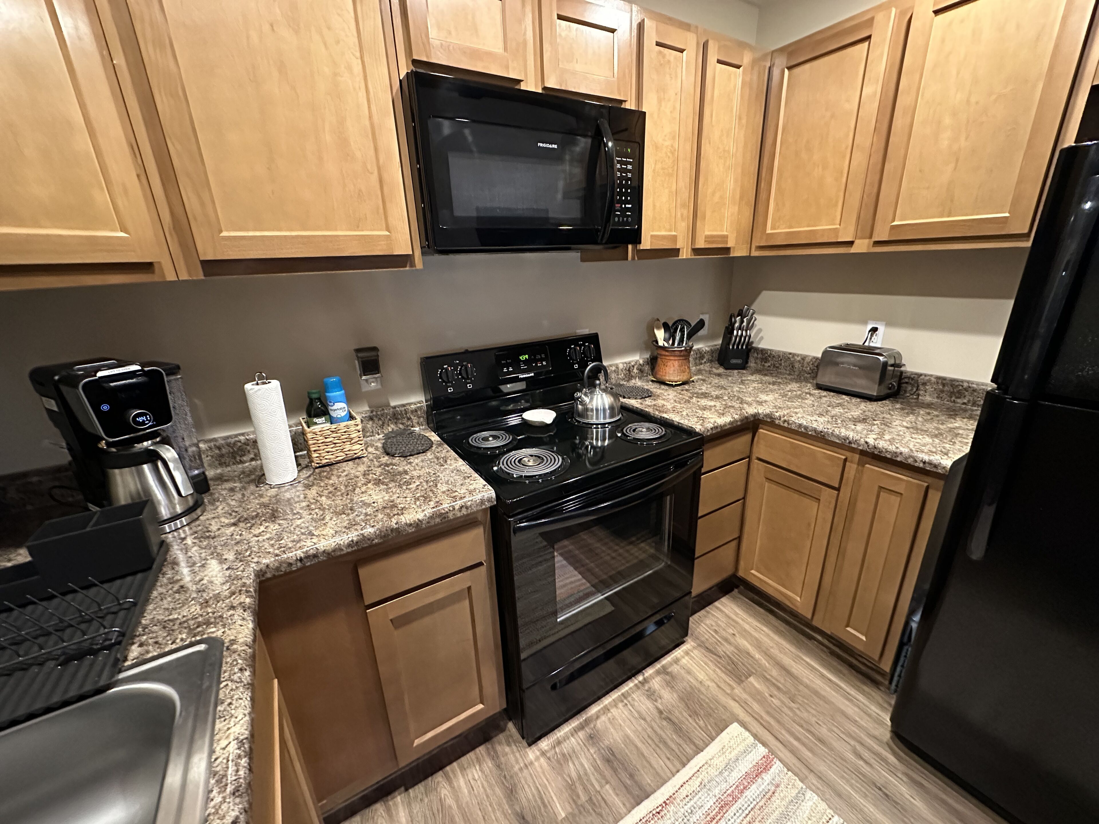 A kitchen with wooden cabinets, a black microwave, a stove, a toaster, and a coffee maker.