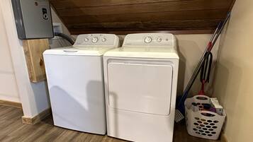 A laundry room with two white front-loading washing machines, a water heater, and a mop leaning against the wall.