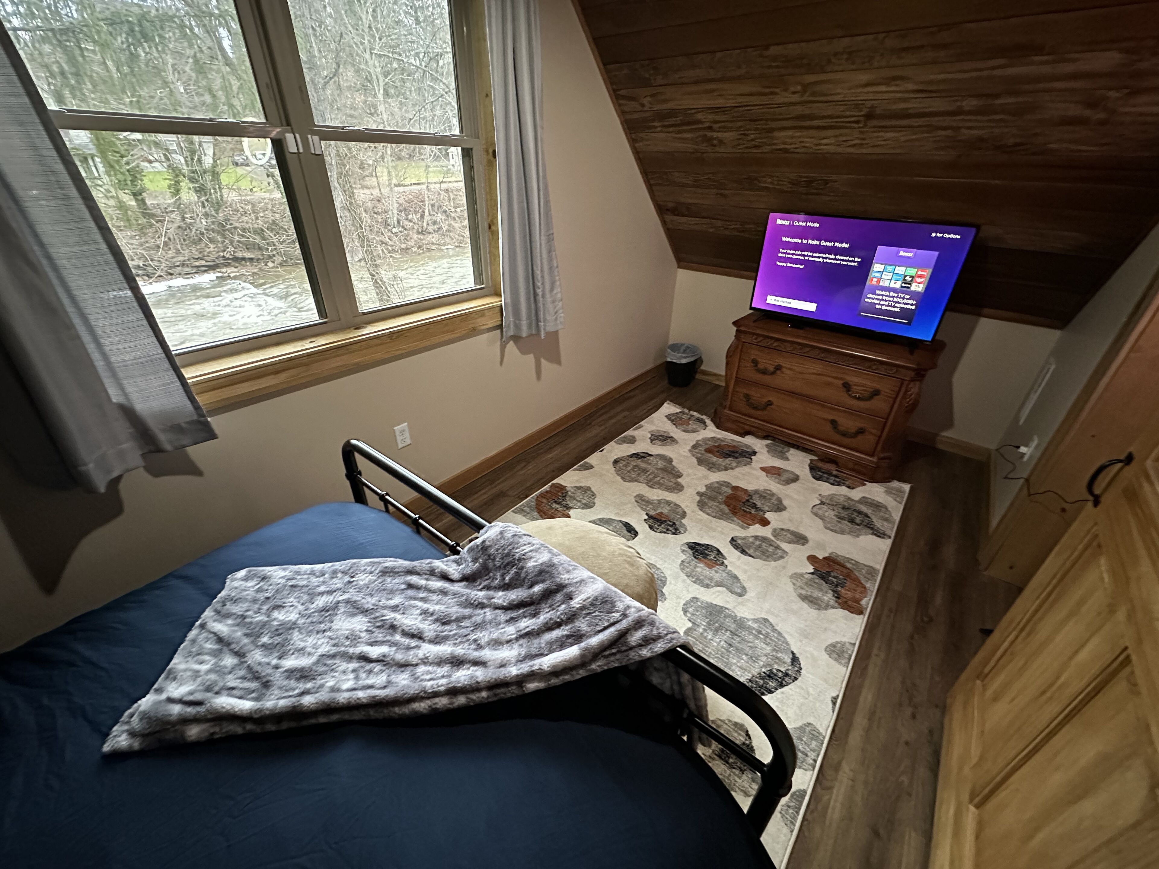Una habitación pequeña y acogedora con una cama individual, un aparador de madera y un televisor mostrando un mensaje de bienvenida.