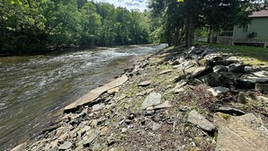 A riverside view with a rocky shoreline, trees, and a house in the background. - Parsons Riverside Retreat: Steps away from a rolling mountain stream and trails (Parsons)