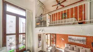 Et niveaudelt opholdsrum med balkon, sofa og spiseområde.