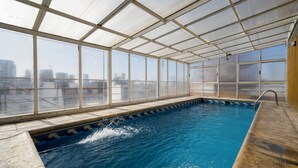 En indendørs swimmingpool med udsigt over byen gennem store vinduer.