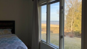 Une chambre avec une grande fenêtre, un lit recouvert d’une literie à motifs, et une vue sur un champ verdoyant et des arbres.
