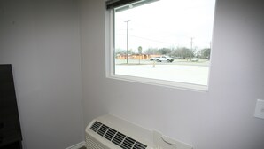A room with a window, a wall-mounted air conditioner, and a view of a parking lot. - Edna Star Motel & Laundry (Edna)