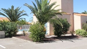 A building with a beige exterior and a tiled roof. There are palm trees and other greenery in front of the building.