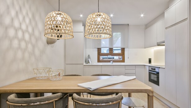 Une cuisine moderne avec des meubles blancs, une table à manger en bois et deux lampes suspendues.