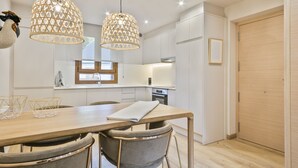 Une cuisine moderne avec des meubles blancs, une table à manger en bois et deux lampes suspendues.