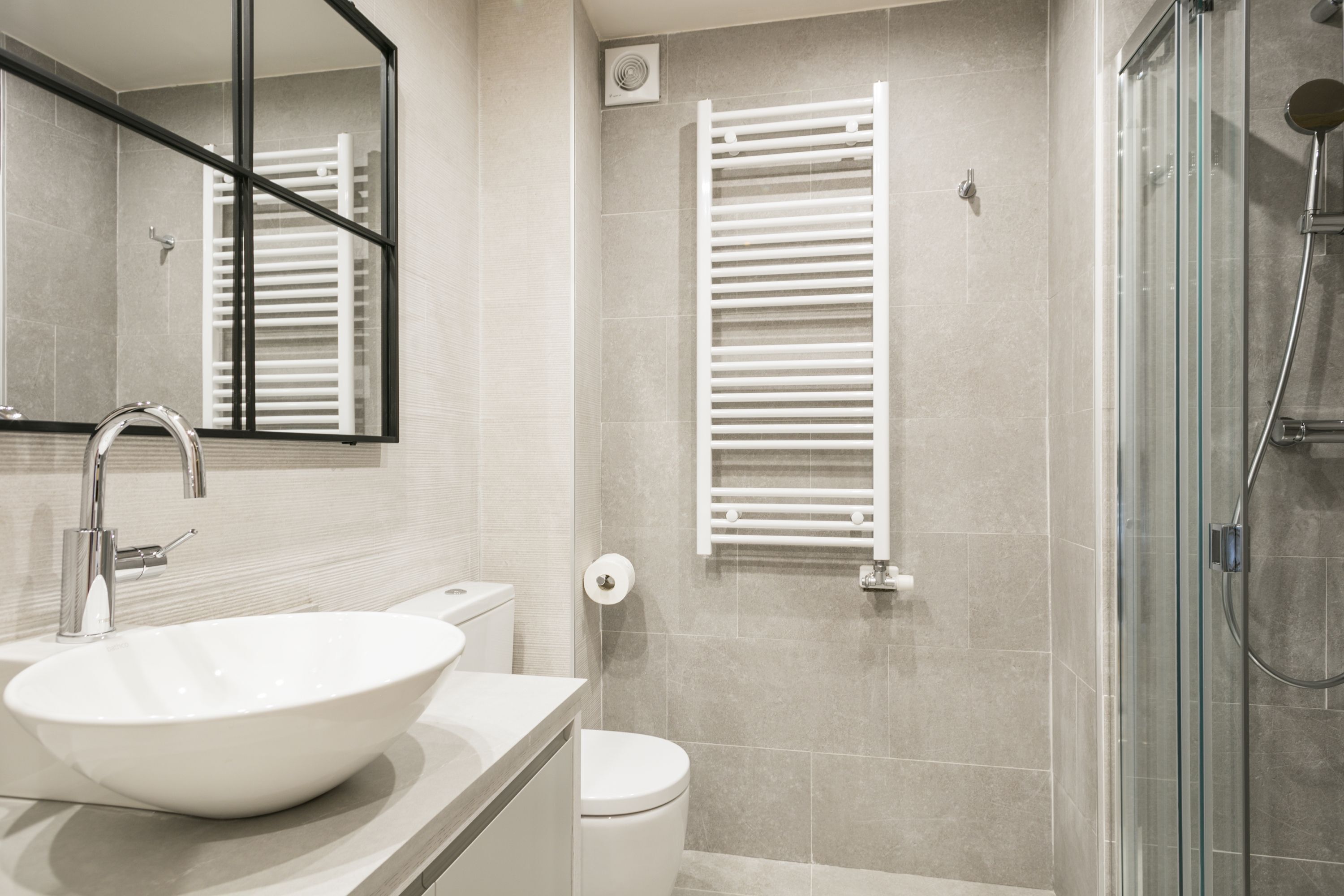 Een moderne badkamer met een groot wit wastafelmeubel, een toilet, een douchecabine met glazen wanden en een handdoekrek.