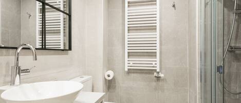 Een moderne badkamer met een groot wit wastafelmeubel, een toilet, een douchecabine met glazen wanden en een handdoekrek.