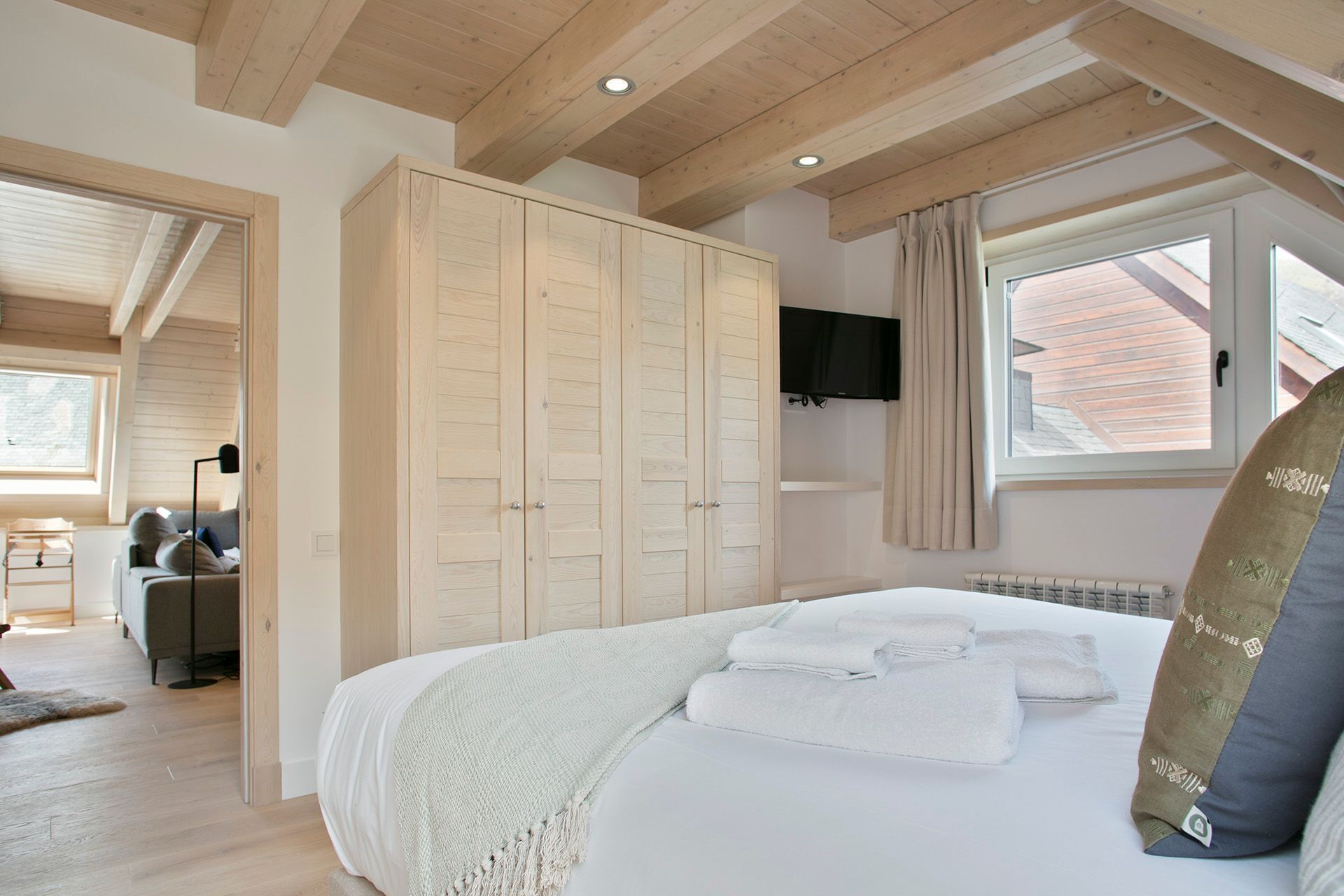 Een slaapkamer met een groot bed, een houten garderobe, een flatscreen televisie en een raam met gordijnen.