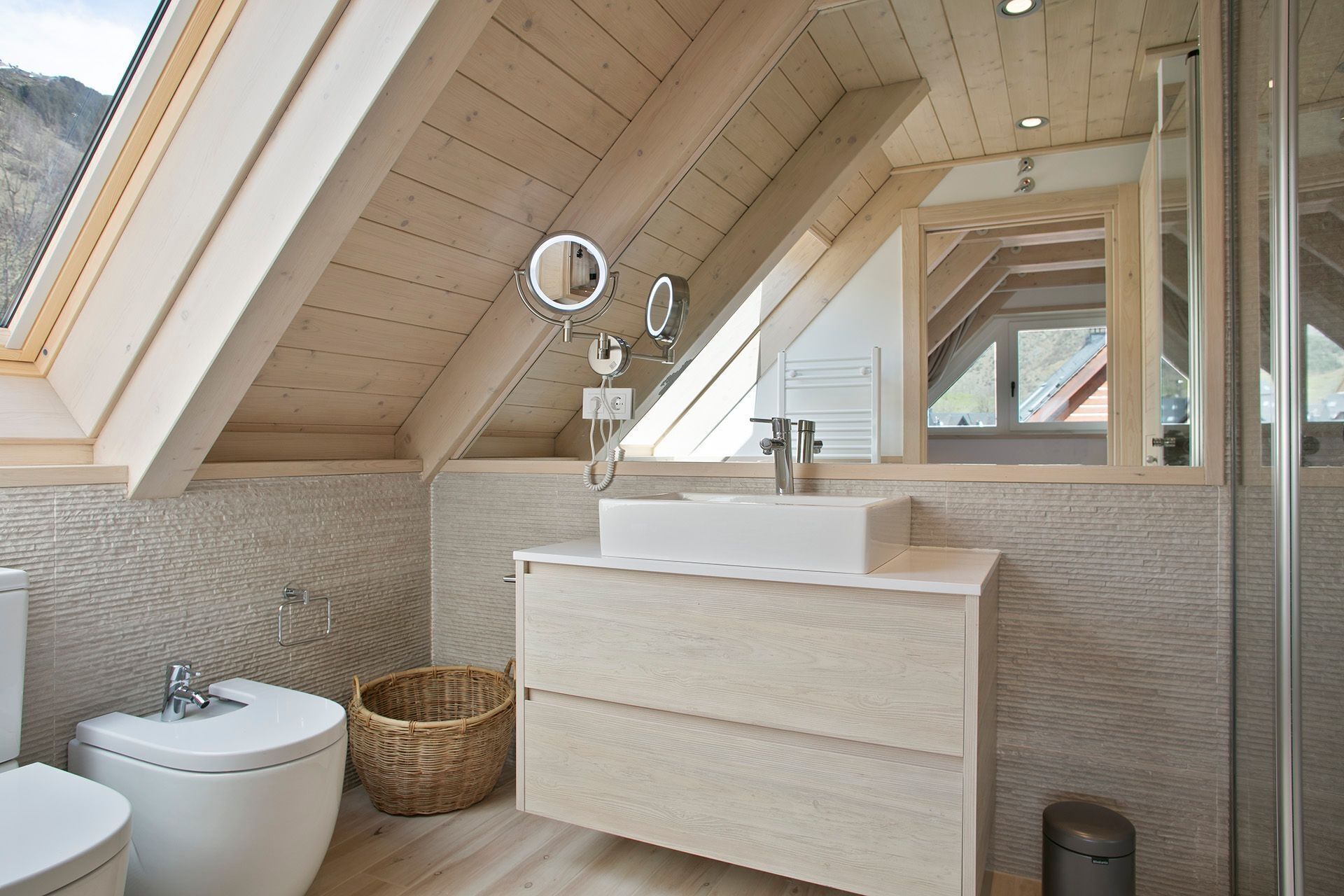 Ein modernes Badezimmer mit Dachfenster, einem großen Spiegel, einem Waschbecken und einer Toilette.