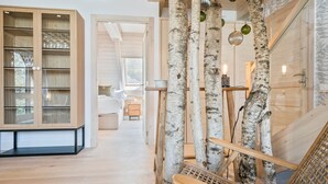 Um interior moderno com réplicas de bétulas, um armário de madeira com portas de vidro e uma área de estar acolhedora.