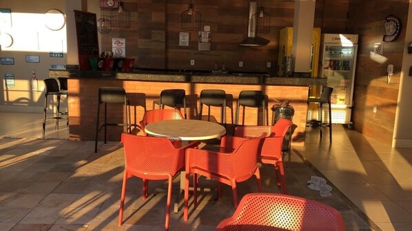 A restaurant with a round table and red chairs, a counter with stools, and a refrigerator in the background. - Santuario Palace Hotel (Aparecida)