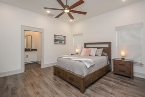 A bedroom with a wooden bed, a ceiling fan, a nightstand, and a window with blinds. - Luxury Lakefront Home w/ Overhanging Deck + Kayaks (Willis)