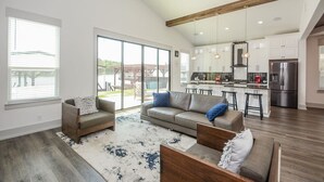 Ein geräumiges Wohnzimmer mit einer großen Couch, einem Couchtisch und einem Essbereich mit einer Bar. Es gibt eine Küche mit modernen Geräten und ein großes Fenster mit Blick auf eine Terrasse.