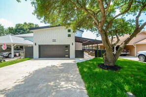 A modern two-story house with a garage, a covered patio, and a well-maintained lawn. - Luxury Lakefront Home w/ Overhanging Deck + Kayaks (Willis)