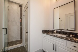 A bathroom with a glass shower enclosure, a sink with a marble countertop, and a large mirror. - Luxury Lakefront Home w/ Overhanging Deck + Kayaks (Willis)