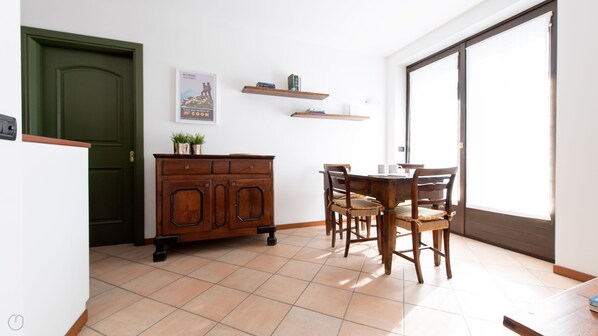 A dining area with a wooden table and chairs, a cabinet with drawers, a green door, and a poster on the wall. - Sertorelli 2 - One Bedroom Apartment, Sleeps 3 (Bormio)